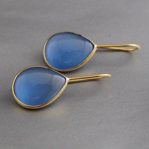 Op de afbeelding: Een paar gouden oorbellen met blauwe stenen in de vorm van een traan.