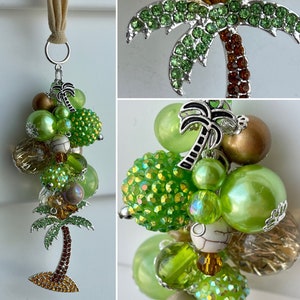 May include: A silver charm with a green and brown palm tree and a cluster of green, brown, and clear beads. The charm is attached to a silver chain.