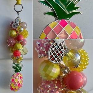 May include: A pineapple-shaped keychain with a silver charm and a beaded chain. The beads are pink, yellow, and clear. The pineapple is pink and yellow with a green top.