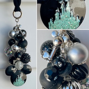 May include: A black and silver charm bracelet with a Mickey Mouse charm featuring a green glitter castle. The bracelet also includes black, silver, and iridescent beads.