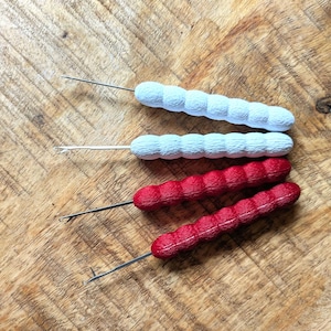 May include: Four crochet hooks with textured handles. Two are light blue, and two are red. The hooks are arranged on a wooden surface, showcasing the tools' design and color variations. The hooks are for crafting.