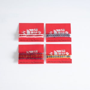 Peut inclure: Quatre bracelets tissés de différentes couleurs, présentés sur des cartes rouges. Les bracelets présentent des motifs rouges, blancs, bleus et jaunes. Chaque carte a un motif découpé et l'adresse www.etsy.com/nl/shop/Domdamsstore.