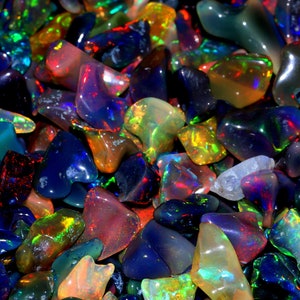 Può includere: Una vista ravvicinata di una collezione di pietre preziose di opale colorate. Gli opali sono di varie forme e dimensioni, con colori iridescenti di blu, verde, rosso e giallo.