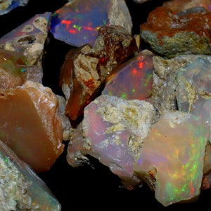 May include: A collection of rough opal stones in various shades of brown, white, and gray with iridescent flashes of color. The stones are irregular in shape and have a natural, unpolished appearance.