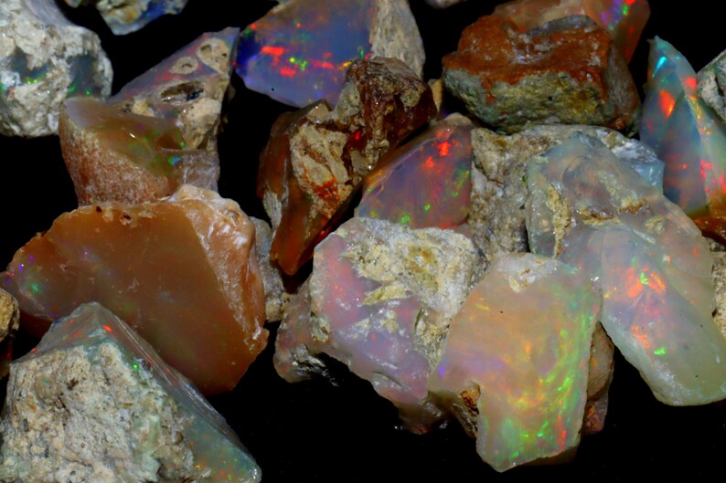 May include: A collection of rough opal stones in various shades of brown, white, and gray with iridescent flashes of color. The stones are irregular in shape and have a natural, unpolished appearance.