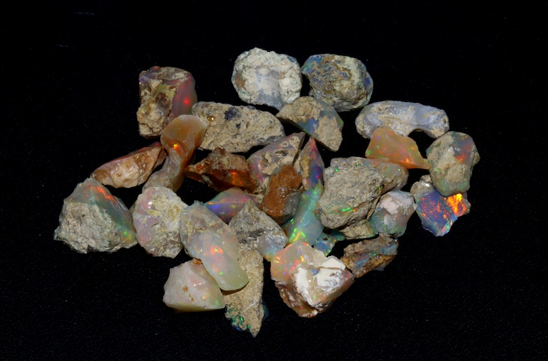 May include: A collection of rough opal stones in various shades of brown, white, and grey with iridescent flashes of color. The stones are irregular in shape and size.