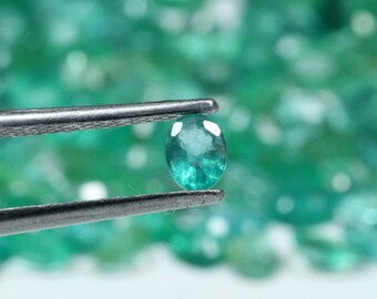 May include: A vibrant green emerald gemstone held in tweezers, with a background of many similar gemstones.