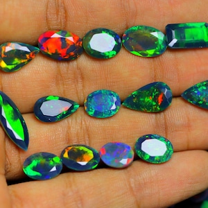 May include: A collection of twelve faceted loose opals in various shapes including pear, oval, marquise, and rectangular cuts. These gemstones display dark base tones with vibrant flashes of green, red, orange, and blue color play throughout.
