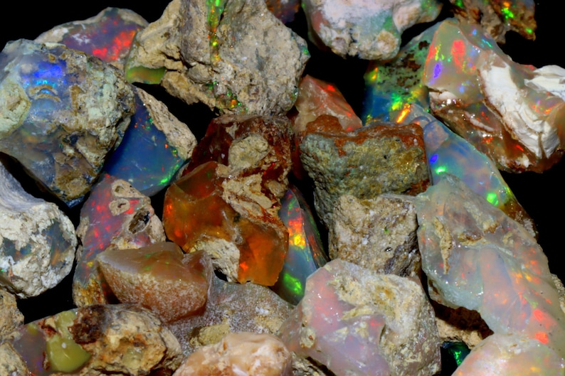 May include: A collection of rough opal stones in various shades of brown, gray, and white with iridescent flashes of color. The stones are irregular in shape and have a natural, unpolished appearance.