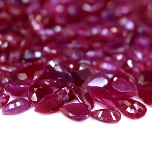 May include: A close-up of a pile of loose, faceted ruby gemstones. The rubies are a deep red colour and have a pear shape.