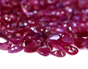 Puede incluir: Primer plano de un montón de piedras preciosas de rubí facetadas sueltas. Los rubíes son de color rojo intenso y tienen forma de pera.