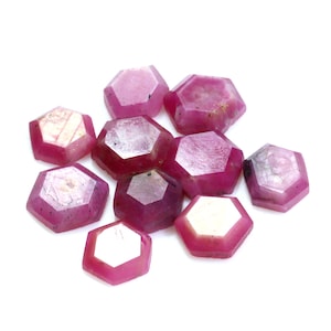 Peut inclure: Dix pierres précieuses de rubis rose facettées, chacune de forme hexagonale, sont éparpillées sur un fond blanc.