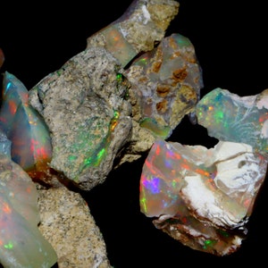 May include: A collection of rough opal stones with iridescent colors, including green, blue, red, and orange. The stones are embedded in a gray, brown, and white matrix.