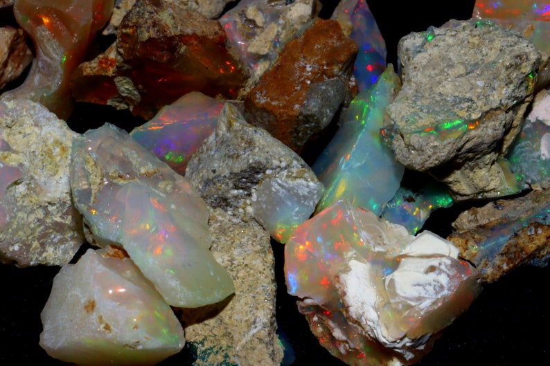 May include: A collection of rough opal stones in various sizes and shapes. The opals are a milky white with flashes of iridescent color, including green, blue, and red.