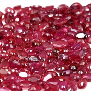 May include: A large collection of loose, faceted ruby gemstones. The rubies are various shades of red and have a glossy finish.