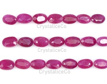 May include: A row of 15 oval-shaped, faceted ruby gemstones, arranged in three rows of five. The gemstones are a deep pink color and have a glossy finish.
