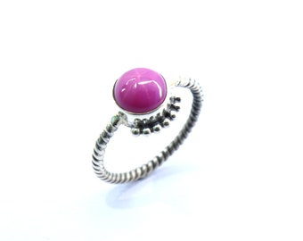 Puede incluir: Un anillo de plata con una piedra preciosa de zafiro estrellado rosa. El anillo tiene una banda retorcida y un diseño de cuentas alrededor de la piedra.