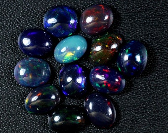Puede incluir: Una colección de 12 opales negras de forma ovalada con colores iridiscentes, incluyendo azul, verde, rojo y morado.