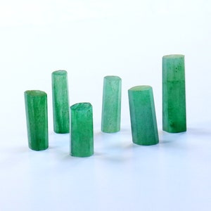 May include: Six green gemstone cylinders of varying sizes and shapes, arranged on a white surface.
