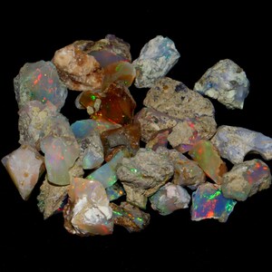 May include: A collection of rough opal stones in various shades of white, gray, and brown with iridescent flashes of color. The stones are of different sizes and shapes, and some have a rough, textured surface.