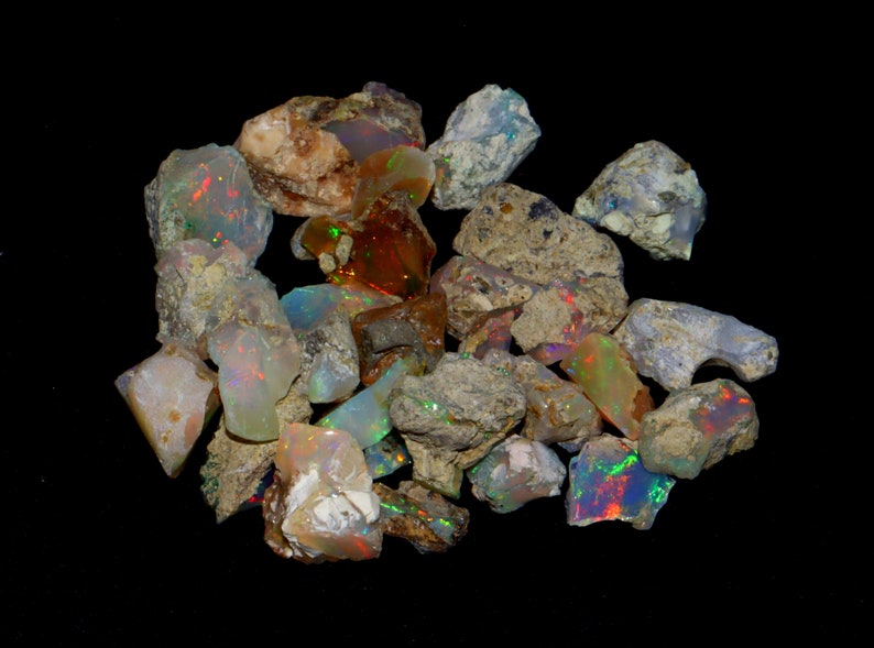 May include: A collection of rough opal stones in various shades of white, gray, and brown with iridescent flashes of color. The stones are of different sizes and shapes, and some have a rough, textured surface.