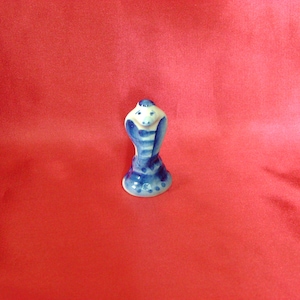 Puede incluir: Una peque&ntilde;a figurita de cer&aacute;mica de una cobra azul y blanca con la capucha levantada. La figurita est&aacute; pintada en un estilo ruso tradicional.