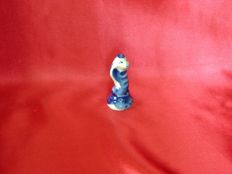 Puede incluir: Una peque&ntilde;a figurita de cer&aacute;mica de una serpiente azul y blanca con la cabeza levantada, de pie sobre una base. La figurita est&aacute; pintada en un estilo tradicional.
