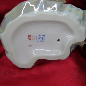 Puede incluir: La parte inferior de una figurita de porcelana con una marca azul y blanca que dice "Made in USSR" y el n&uacute;mero "122P".