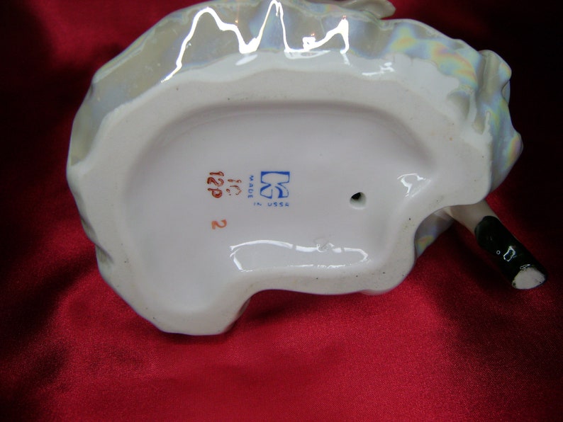 Puede incluir: La parte inferior de una figurita de porcelana con una marca azul y blanca que dice "Made in USSR" y el n&uacute;mero "122P".