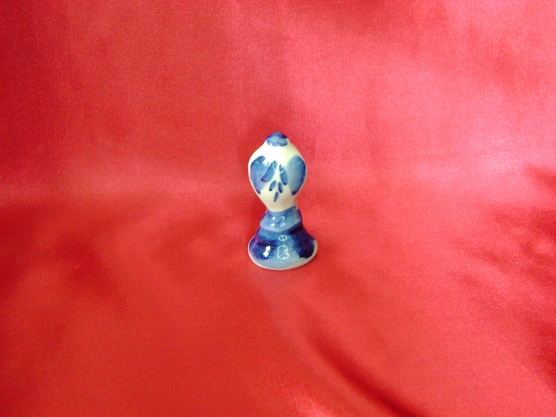 Puede incluir: Un peque&ntilde;o tap&oacute;n de botella de cer&aacute;mica blanca con un dise&ntilde;o floral azul y blanco. El tap&oacute;n tiene forma de campana con la parte superior redondeada.