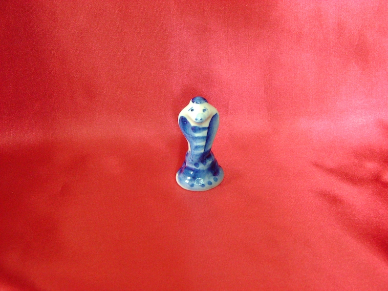 Puede incluir: Una peque&ntilde;a figurita de cer&aacute;mica de una cobra azul y blanca con la capucha levantada. La figurita est&aacute; pintada en un estilo ruso tradicional.