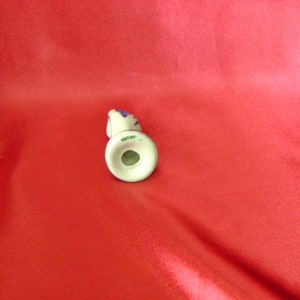 Puede incluir: Una figurita de cer&aacute;mica blanca de una mujer con detalles azules y verdes. La figurita est&aacute; de pie sobre una base blanca con un agujero en el centro.