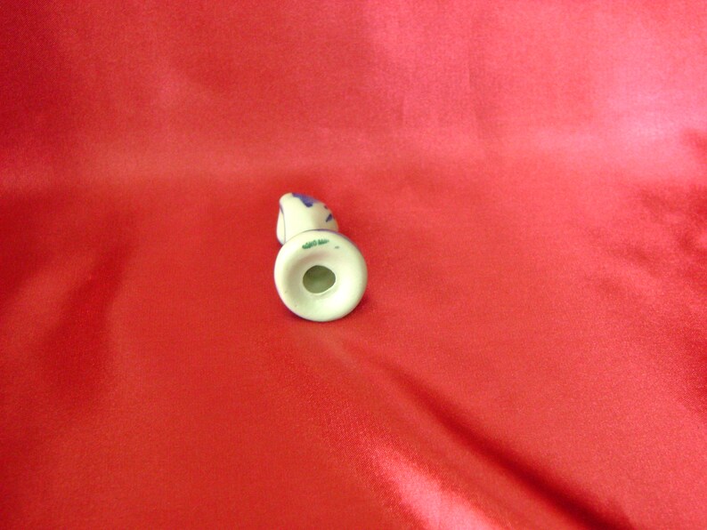 Puede incluir: Una figurita de cer&aacute;mica blanca de una mujer con detalles azules y verdes. La figurita est&aacute; de pie sobre una base blanca con un agujero en el centro.