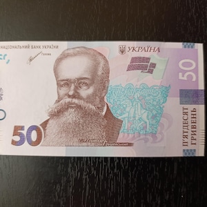 May include: A Ukrainian 50-hryvnia banknote featuring a portrait of Mykhailo Hrushevskyi. The bill has a light blue and purple design with Ukrainian text. The number 50 is prominently displayed on the bill.
