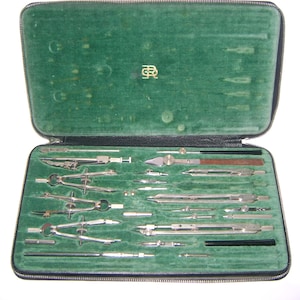 Może przedstawiać: Otwarty, zabytkowy zestaw do rysowania w czarnym etui z zielonym aksamitnym wnętrzem. Zestaw zawiera różne srebrne cyrkle, dzielniki i inne narzędzia do rysowania. Etui jest zapinane na zamek i ma złoty emblemat.