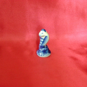 Puede incluir: Una figurita de cer&aacute;mica azul y blanca de una cobra con la cabeza levantada, la serpiente est&aacute; enroscada en una base.