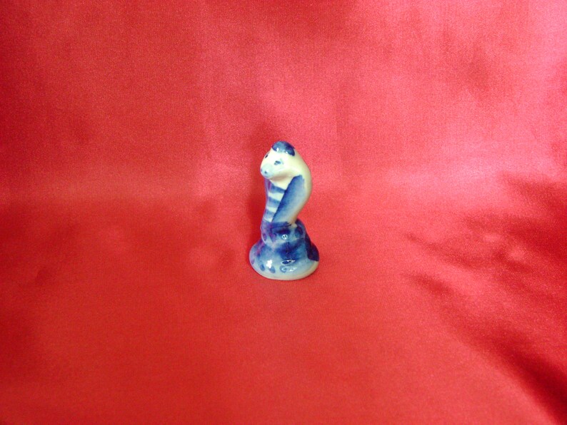 Puede incluir: Una figurita de cer&aacute;mica azul y blanca de una cobra con la cabeza levantada, la serpiente est&aacute; enroscada en una base.
