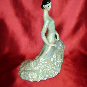 Puede incluir: Una figurita de porcelana de una mujer con un vestido fluido e iridiscente. La mujer est&aacute; en una posici&oacute;n de baile con los brazos extendidos. La figurita es de estilo espa&ntilde;ol tradicional.