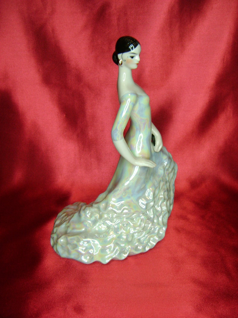 Puede incluir: Una figurita de porcelana de una mujer con un vestido fluido e iridiscente. La mujer est&aacute; en una posici&oacute;n de baile con los brazos extendidos. La figurita es de estilo espa&ntilde;ol tradicional.