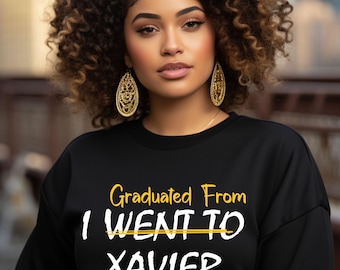 May include: Black sweatshirt with the text "Graduated From I WENT TO XAVIER" in yellow with a line through "WENT TO" and a green and yellow logo with the letters "XU" below the text.