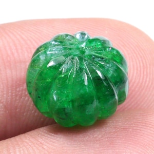 May include: A deep green, faceted, carved gemstone bead in the shape of a pumpkin. The bead is smooth and polished.