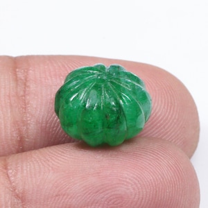May include: A carved, vibrant green gemstone shaped like a pumpkin. The gemstone has detailed ridges and a small stem, showcasing the intricate craftsmanship. The pumpkin is held between two fingers, highlighting its size and detail.