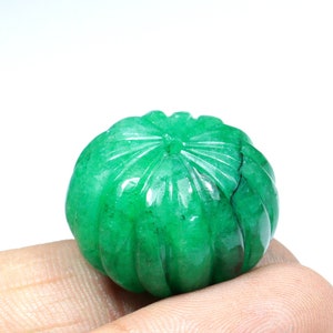 May include: A carved green emerald gemstone, shaped like a sphere with a flower-like design on the top.