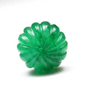 May include: A bright green emerald gemstone carved into a flower shape. The gemstone is faceted and has a smooth, polished finish.