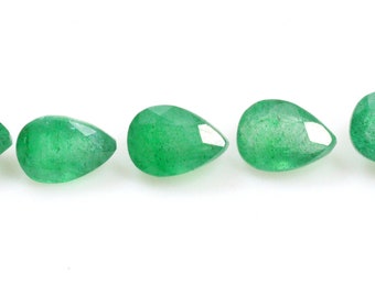 Puede incluir: Cinco gemas verdes facetadas en forma de pera están dispuestas en fila sobre un fondo blanco. Las gemas tienen un aspecto brillante y translúcido, con estructuras internas visibles. El corte de las piedras crea múltiples superficies reflectantes.