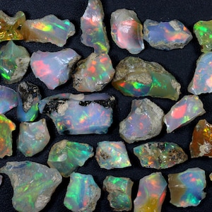 May include: A collection of rough opal stones in various shades of green, blue, and red. The stones are iridescent and have a natural, unpolished look.