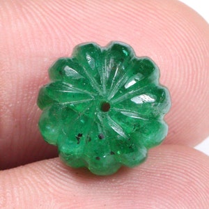 May include: A green emerald gemstone bead with a carved flower design. The bead has a hole drilled through the center for stringing.