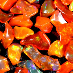 Può includere: Una collezione di pietre preziose di opale arancioni e iridescenti. Le pietre hanno una forma irregolare e una finitura liscia e lucida.