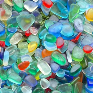 May include: A large collection of smooth, frosted sea glass pieces in a vibrant array of colors including cobalt blue, emerald green, bright red, sunny yellow, and clear white, all featuring rounded edges and a matte, weathered texture.