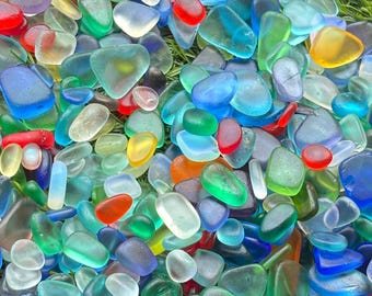 May include: A large collection of smooth, frosted sea glass pieces in a vibrant array of colors including cobalt blue, emerald green, bright red, sunny yellow, and clear white, all featuring rounded edges and a matte, weathered texture.